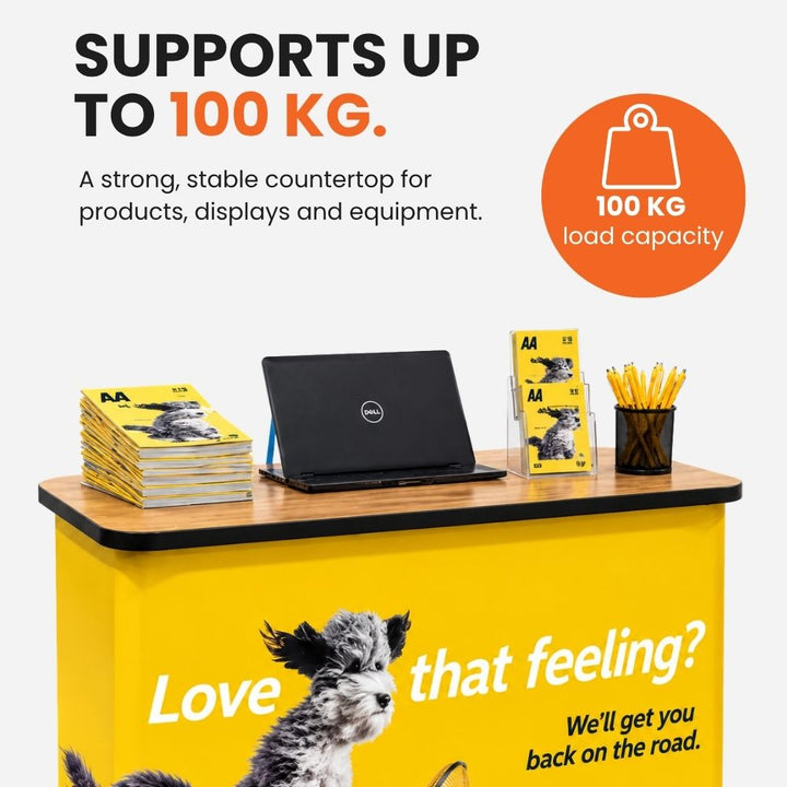 Custom printed event counter supporting brochures, a laptop and literature holder on its countertop, rated to carry up to 100kg.