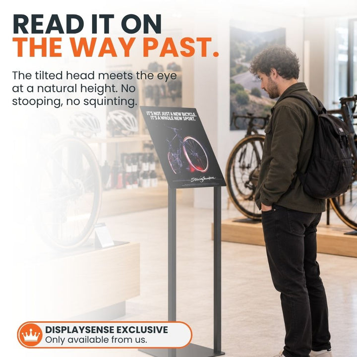 Customer reading an angled A3 freestanding poster stand inside a bicycle shop, demonstrating the raised viewing position of the display.