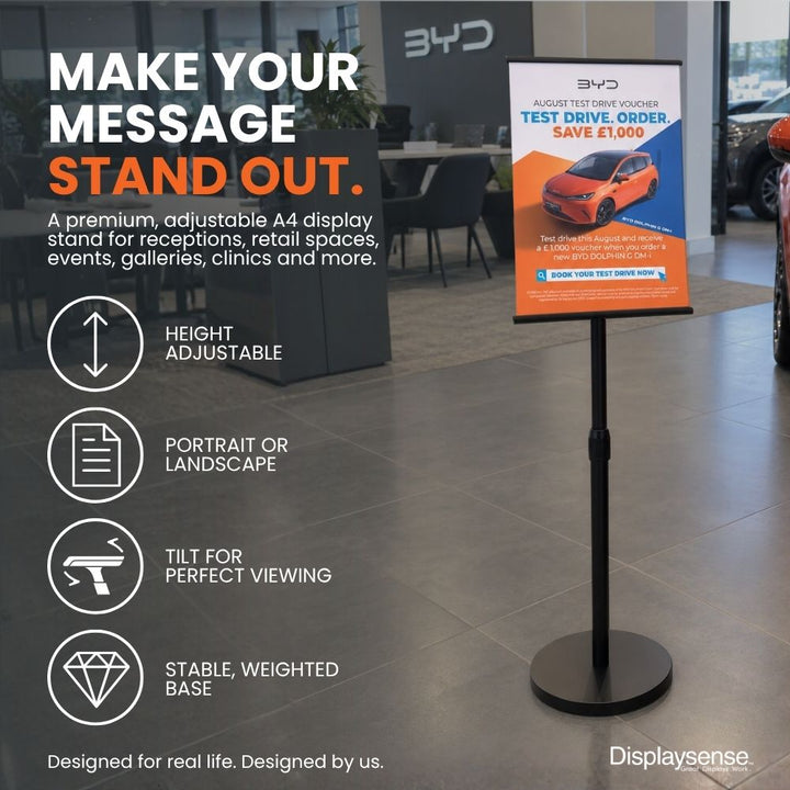 Black A4 freestanding adjustable poster display stand in a showroom, featuring height adjustment, portrait or landscape orientation, tilt adjustment and a weighted base.