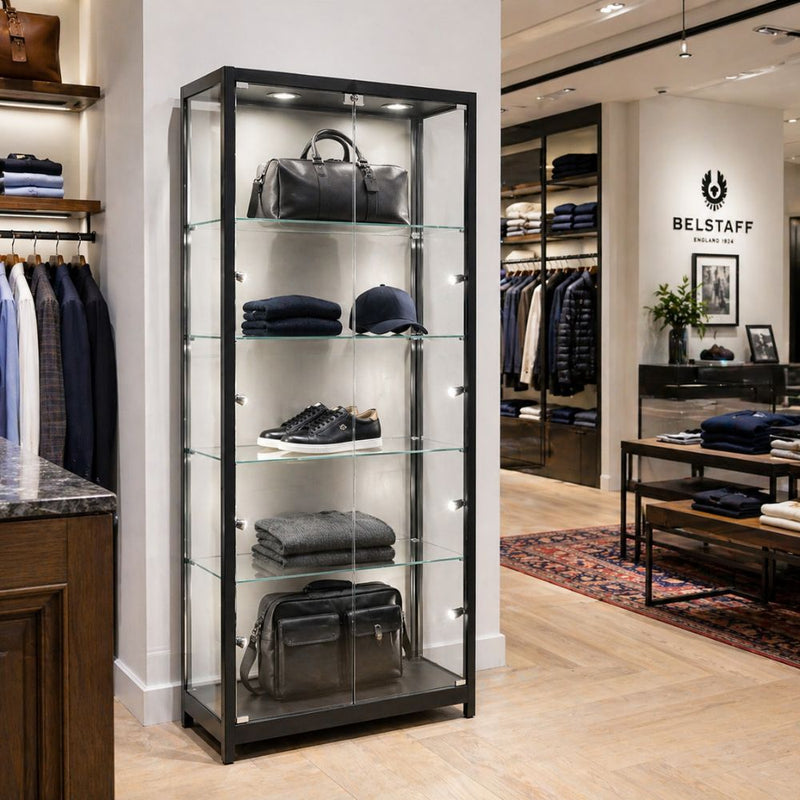 Black aluminium lockable glass display cabinet with LED lighting showcasing bags, shoes and folded clothing in a modern retail shop interior.
