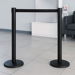 Pair of black barrier posts with black retractable webbing placed in a modern reception area with tiled flooring and minimalist seating.

