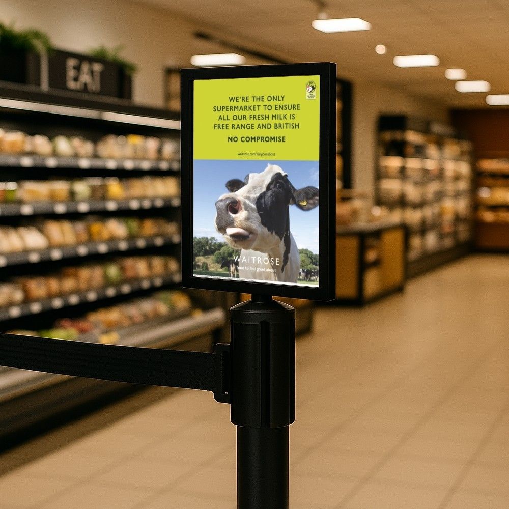  A black barrier sign holder displaying a Waitrose advertisement about British free-range milk in a supermarket aisle.