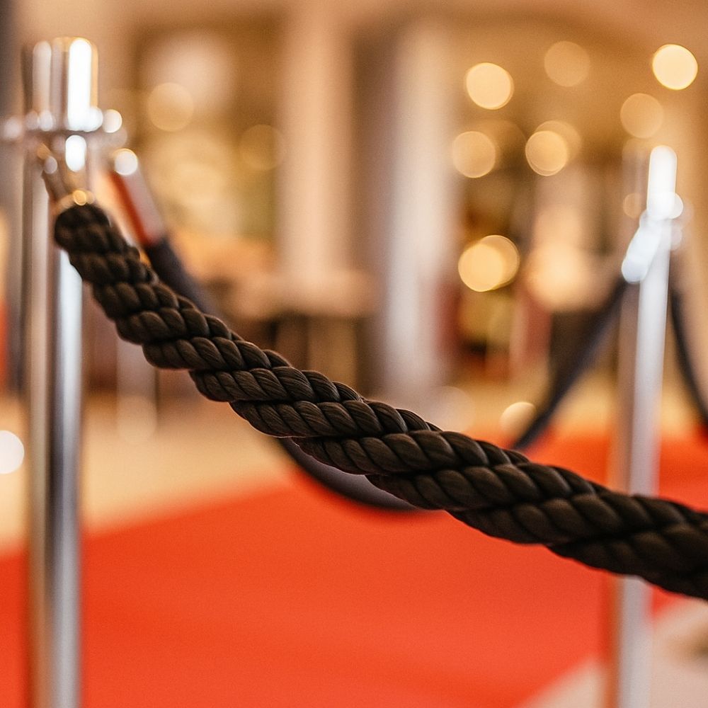 Close-up of a black braided rope barrier with chrome posts on a red carpet, creating a premium entrance area.
