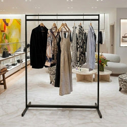 Black freestanding clothes rail displaying a selection of dresses, shirts and a blazer in a modern boutique retail interior.