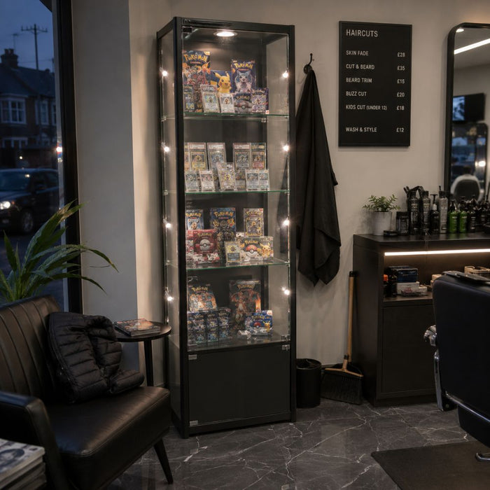 Black illuminated Pokémon card display cabinet in a barbershop