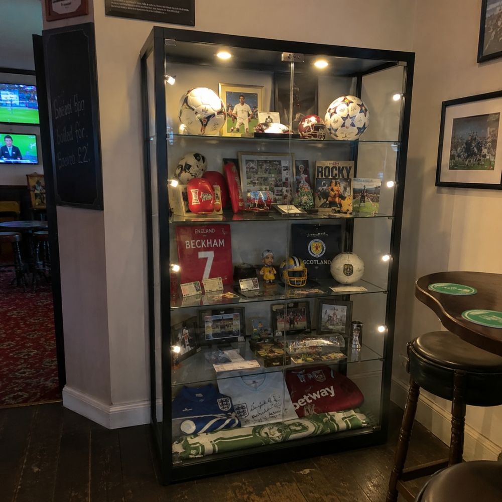 Black illuminated sports memorabilia display cabinet in a pub interior