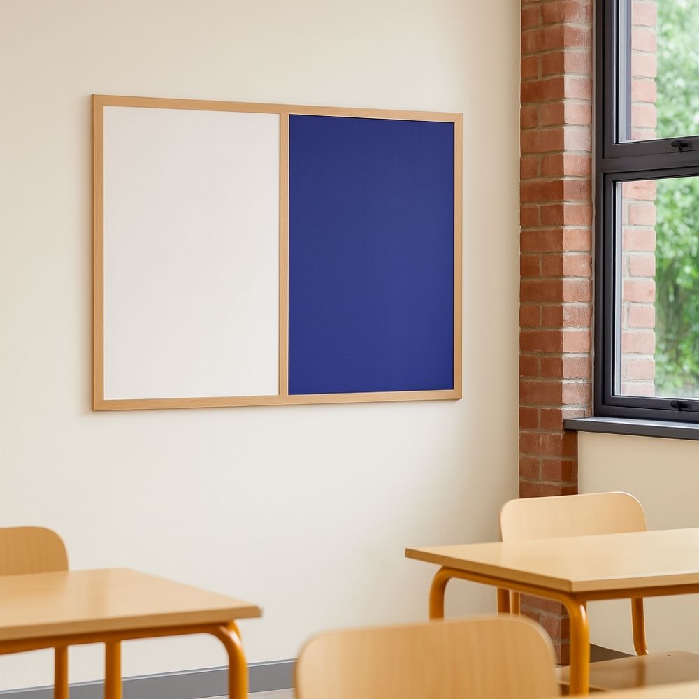 Wall-mounted dual-purpose board with a blue felt noticeboard and white dry-wipe surface in a wooden frame, displayed in a bright classroom with wooden desks and brick-framed window.