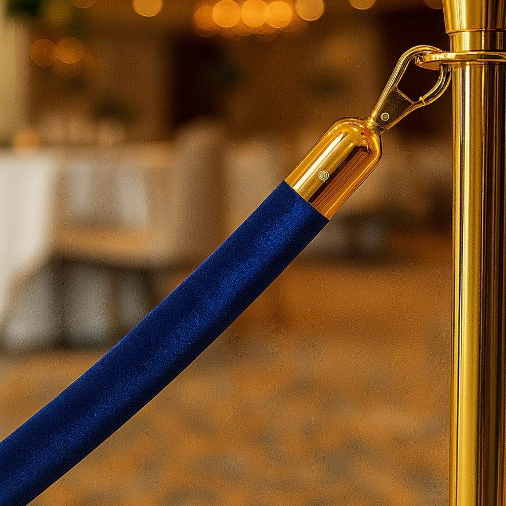 Close-up of a blue velvet barrier rope connected to a gold stanchion post, suitable for luxury events and crowd control.