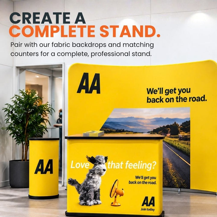 Branded exhibition counter arranged with matching printed display stands and a large fabric backdrop to create a coordinated event space.