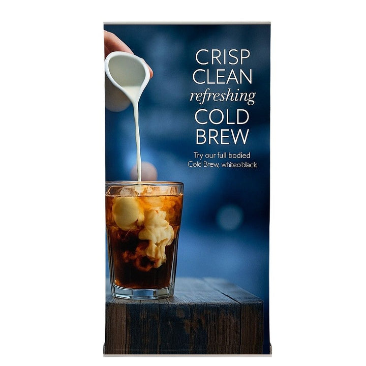 Front-facing view of a roll up banner stand displaying cold brew coffee with milk being poured into a glass, against a gradient blue background and marketing copy promoting a full-bodied brew.

