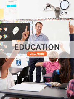 Primary school classroom with male teacher and students raising hands, whiteboard and educational posters in background
