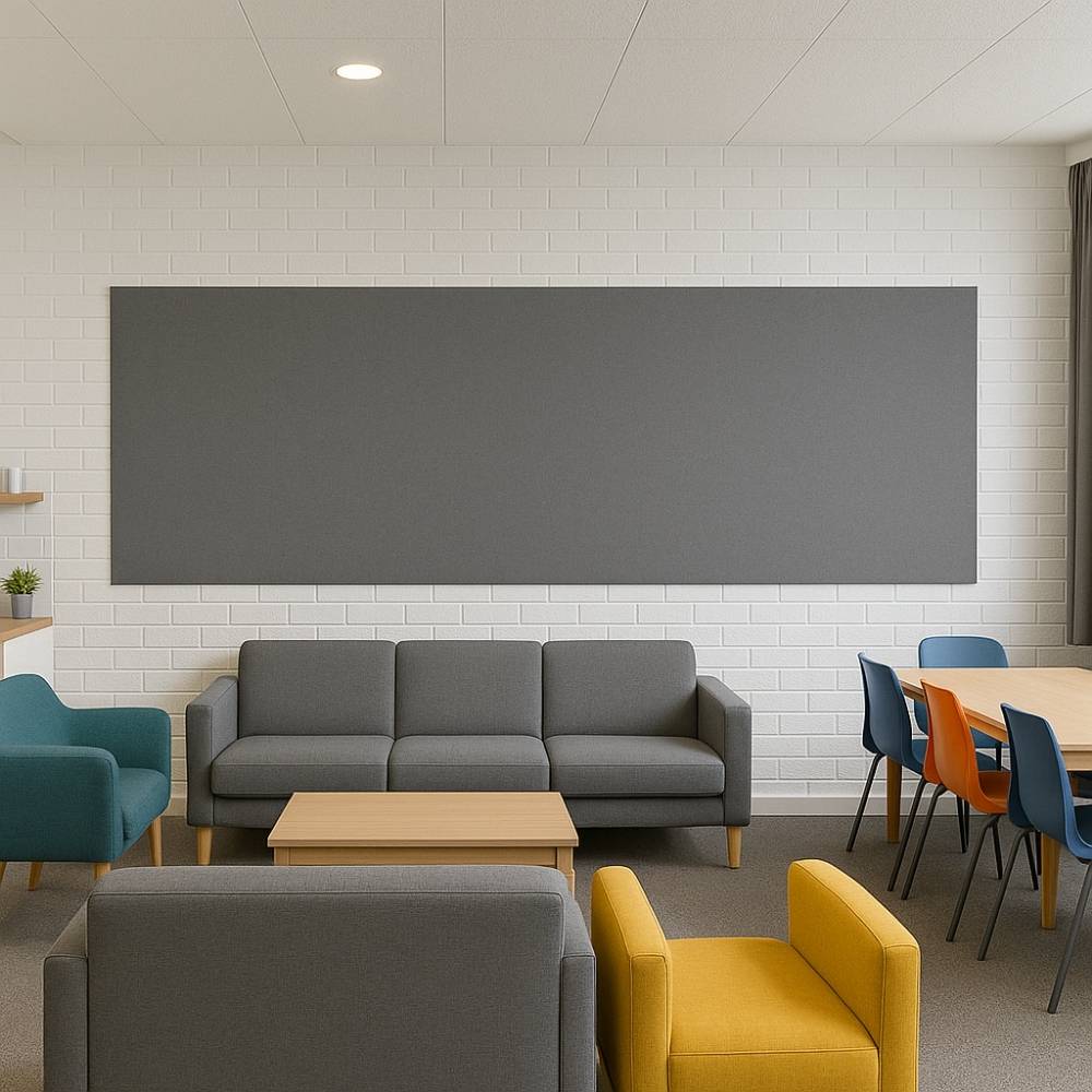 Extra-wide grey felt pinboard mounted on a white brick wall in a modern communal lounge area, featuring grey, teal, and yellow armchairs, a wooden coffee table, and a dining table with colorful chairs.
