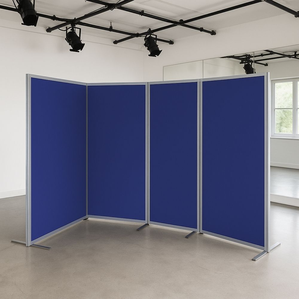 Four-panel room divider with blue fabric and silver aluminium frame, standing on flat metal feet in a dance studio with mirrors, spotlight rigging, and natural light.