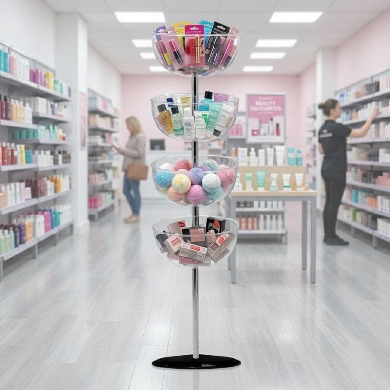 Four-tier acrylic bowl impulse tower loaded with beauty and skincare products, standing in a bright beauty retail shop aisle beside customers browsing.
