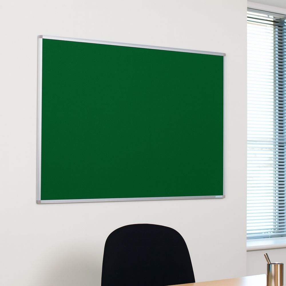 Green felt noticeboard mounted on a white office wall above a black chair and wooden desk.