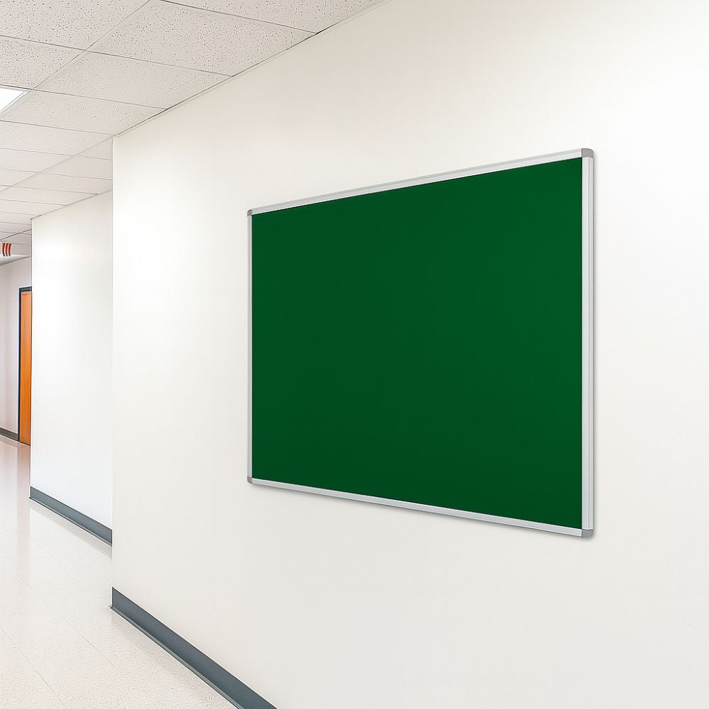 Green noticeboard with silver aluminium frame mounted on a clean white wall in a well-lit school corridor with tiled flooring and ceiling panels.