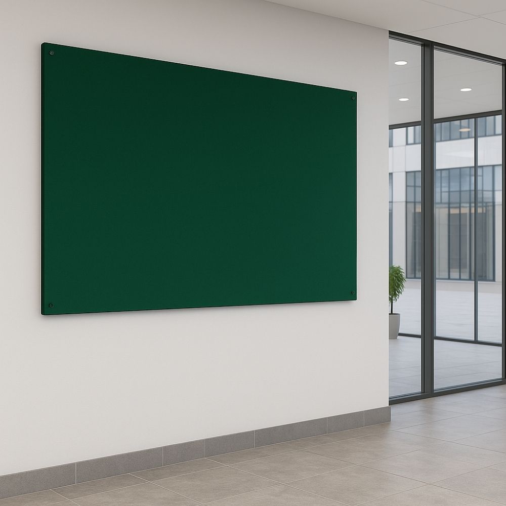 Dark green fabric noticeboard mounted on a clean white wall in a contemporary office corridor with tiled flooring and full-height glass windows overlooking a courtyard.