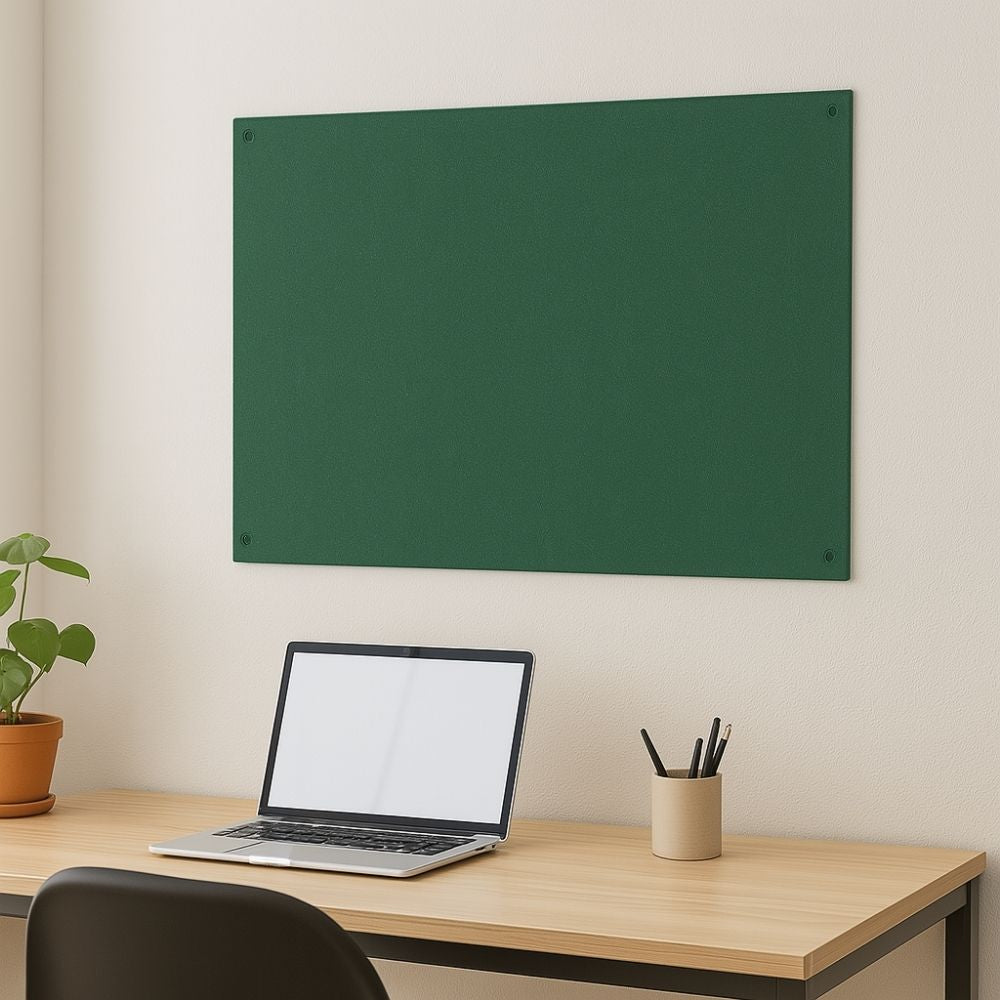 Green fabric pinboard mounted on a cream wall above a light wood desk with a laptop, pencil holder, and potted plant in a minimalist home office setting.
