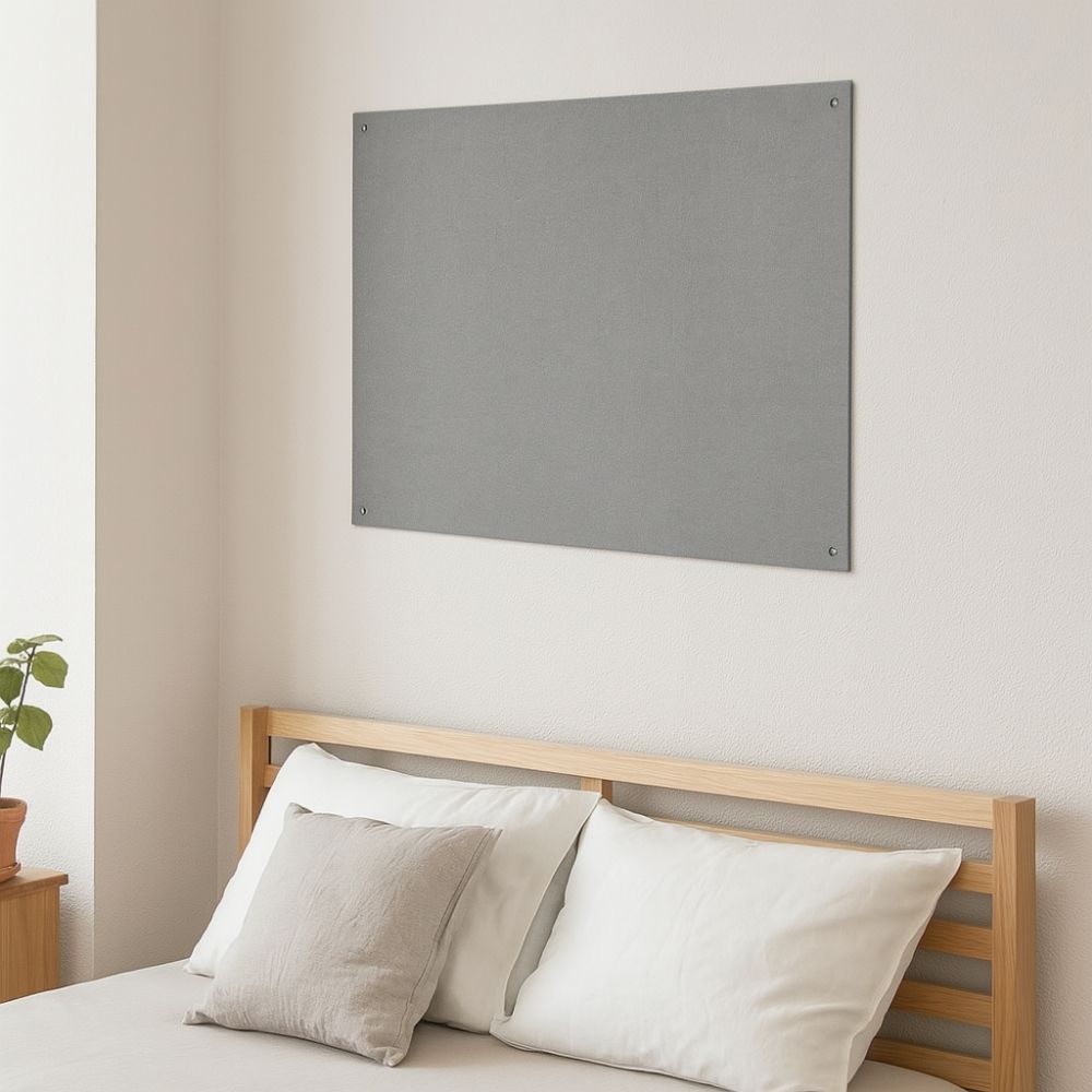 Grey fabric pinboard fixed to a white wall above a light wooden bed with neutral bedding in a minimalist bedroom, featuring a small bedside table and potted plant.