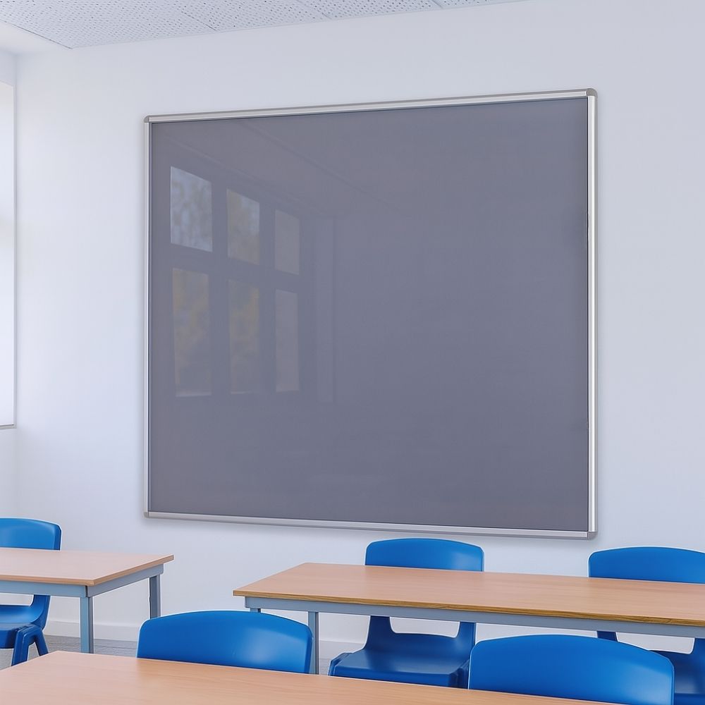 Large grey noticeboard with silver frame mounted on a classroom wall above wooden desks and blue plastic chairs in a bright, modern learning environment.