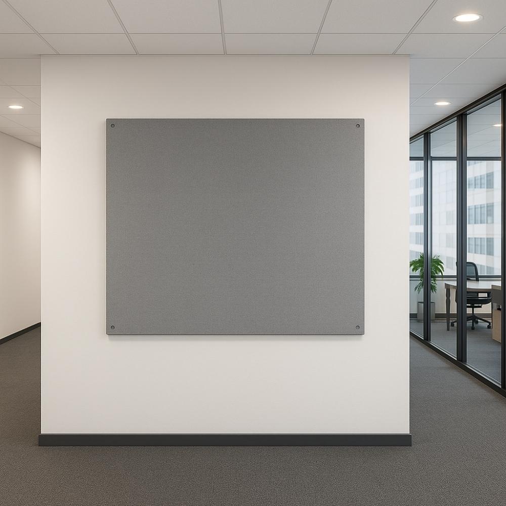 Plain grey fabric noticeboard mounted on a white wall in a contemporary office hallway with carpeted flooring, drop ceiling, and glass-partitioned meeting rooms.
