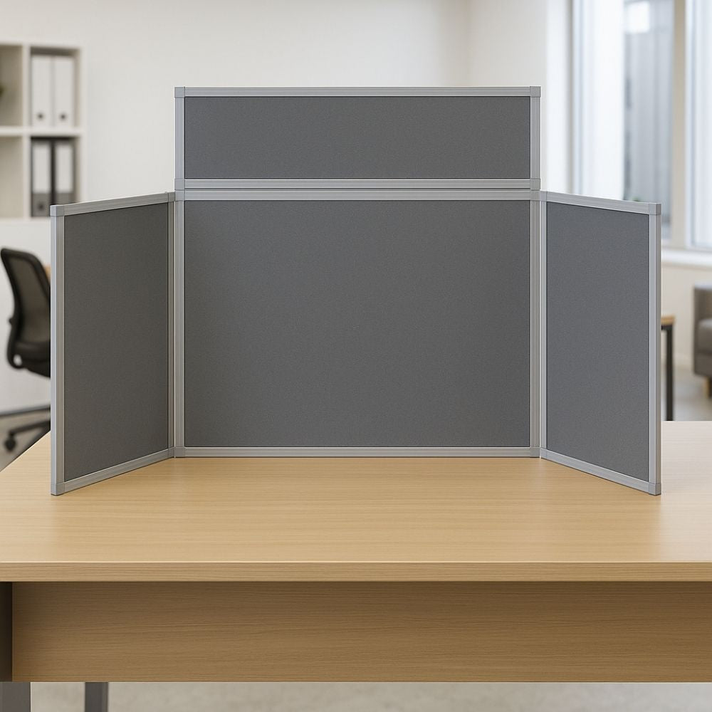 Grey tabletop display board with silver aluminium frame, placed on a wooden office desk in a modern workspace with chairs and shelving in the background.

