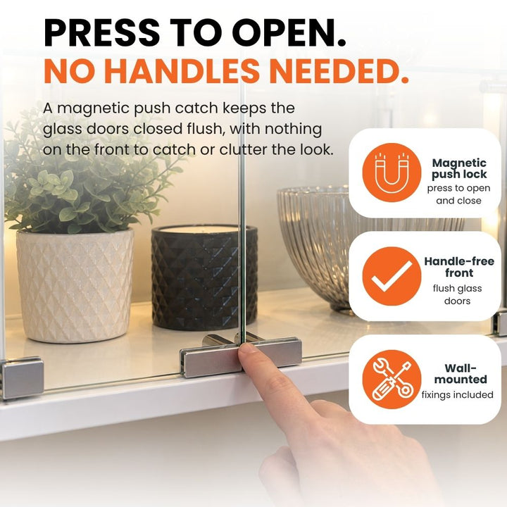 Finger pressing the flush double glass doors to demonstrate the magnetic push-lock mechanism, handle-free front and wall-mounted design.