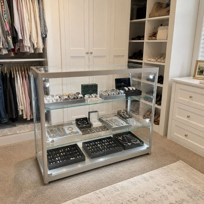 Illuminated glass display cabinet showing luxury watches and jewellery in a walk-in wardrobe