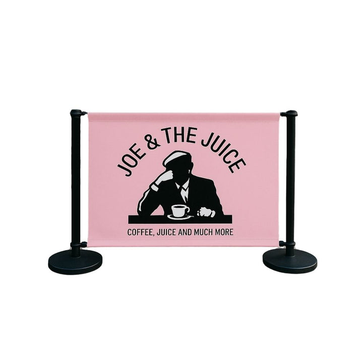 Studio image of Joe & The Juice café barrier featuring pink banner with black silhouette logo and matte black stanchions—designed for hospitality and coffee shop exteriors.


