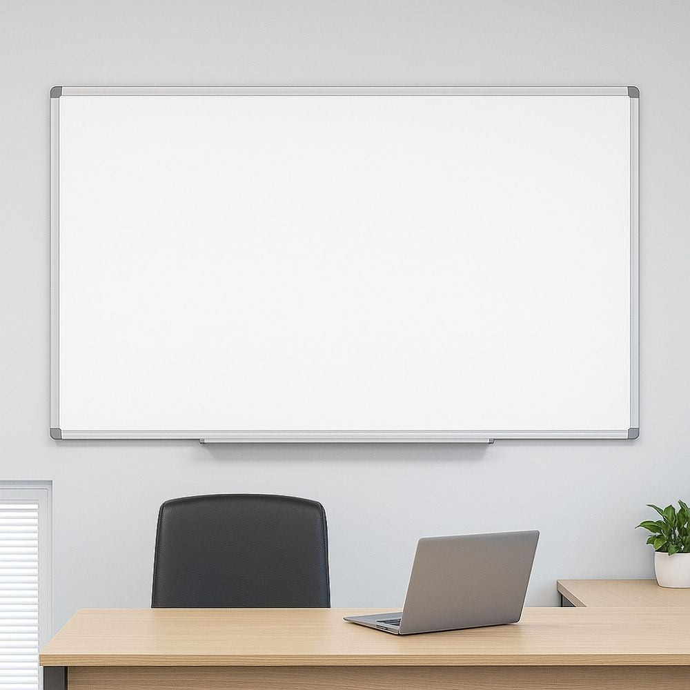 Wall-mounted magnetic dry wipe whiteboard in an office setting above a wooden desk and laptop.