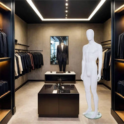 A sleek and modern men's fashion boutique featuring a minimalist interior with dark tones, ambient lighting, and neatly arranged clothing racks displaying premium suits and formalwear. A white male mannequin stands on a round base near the centre, ready for display. In the background, another mannequin dressed in a tailored black suit is positioned in front of a mirror, enhancing the store’s sophisticated aesthetic.
