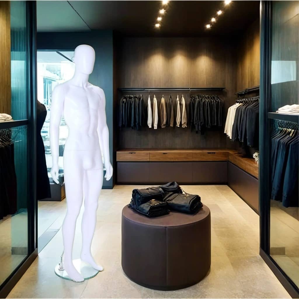 A sleek and modern men's fashion boutique featuring a minimalist design with dark wood paneling, soft lighting, and neatly arranged clothing racks displaying a collection of black, white, and neutral-toned apparel. A glossy white male mannequin stands on a round glass base near the entrance. In the centre, a stylish leather ottoman holds folded black garments, adding to the boutique's sophisticated and contemporary ambiance.