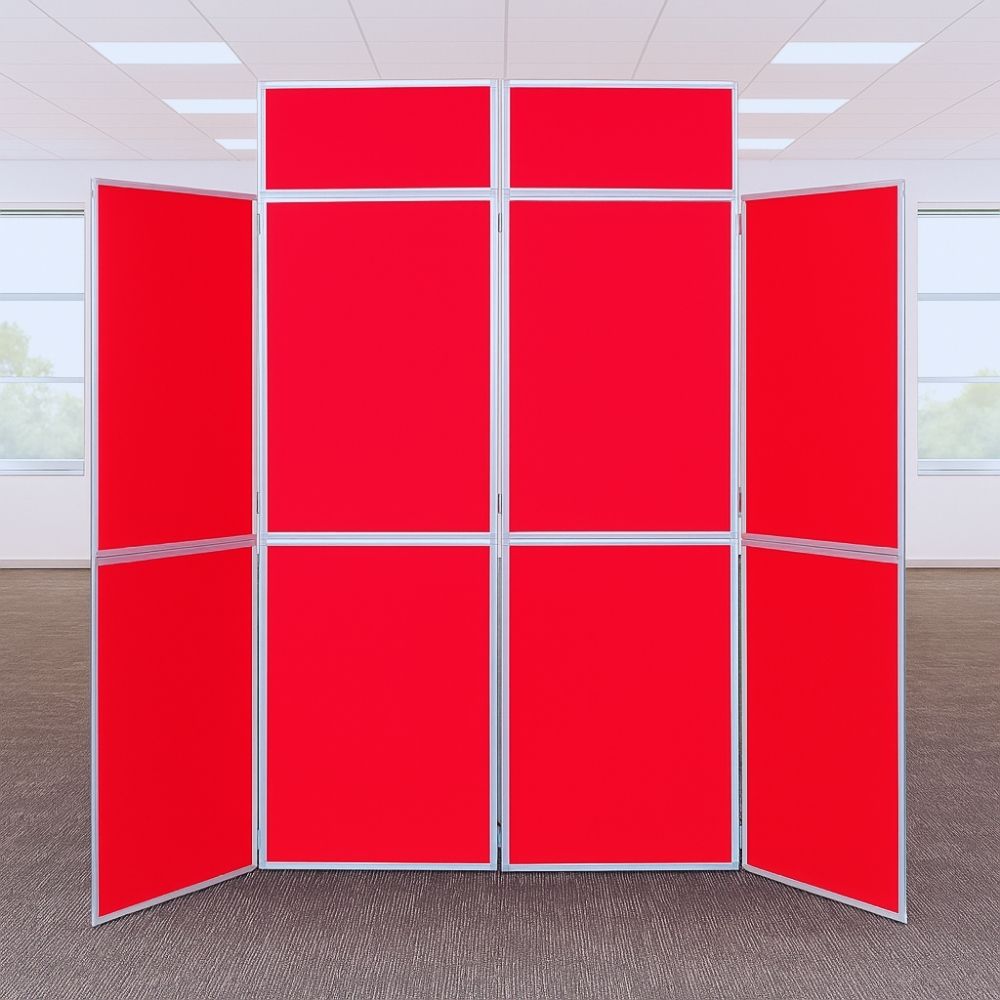 Red eight-panel folding display board with silver frame set up in a bright modern office environment with carpeted flooring and large windows.

