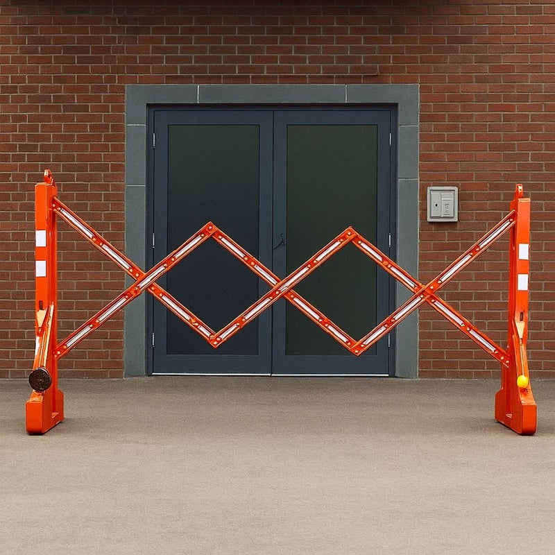 Red reflective expandable safety barrier positioned outside a building entrance with double grey doors.