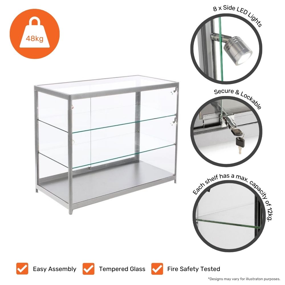 A silver aluminium glass counter display cabinet with a lockable sliding door and tempered glass shelves. The unit features 8 side LED spotlights for improved product visibility. Each shelf has a maximum weight capacity of 12kg, with a total load capacity of 48kg. The design includes easy assembly, fire safety testing, and durable tempered glass. Icons at the bottom highlight these key features.