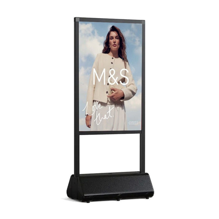 Angled study of the slim black frame, one printed face visible above the moulded water-fillable base that weights the sign on a pavement.
