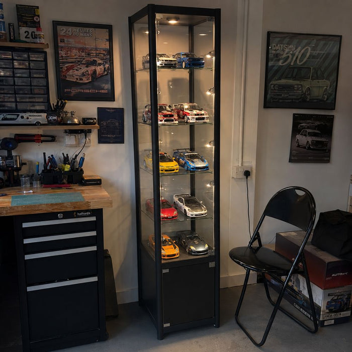 Tall black illuminated glass display cabinet showcasing Porsche and Ferrari diecast model cars