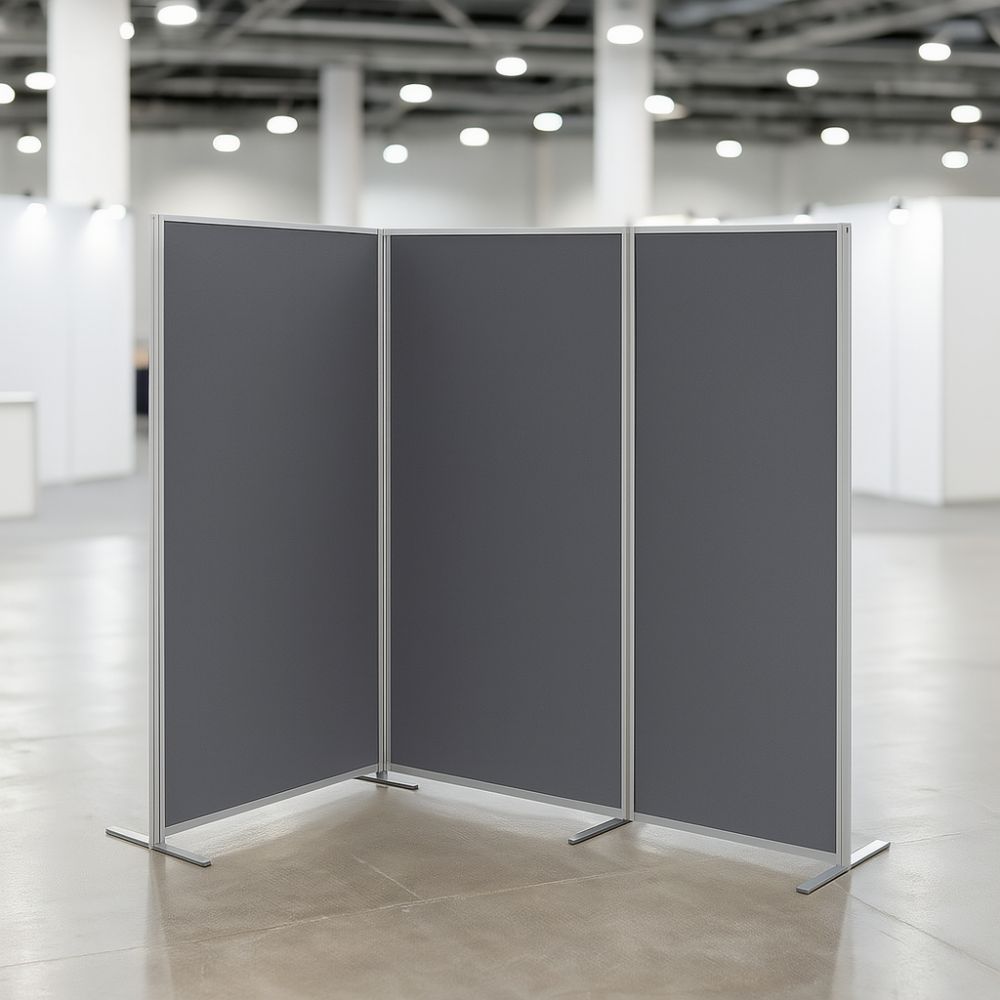 Three-panel room divider with grey felt fabric and silver aluminium frame, set up in a corner formation within a modern exhibition or trade show hall.
