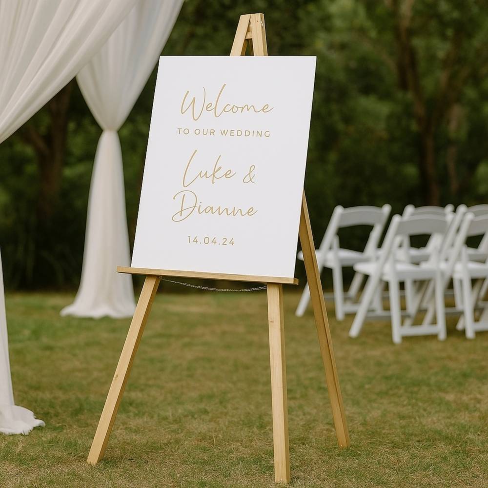 Natural wooden easel standing in an elegant wedding venue with white draped walls, round tables, and floral centrepieces.

