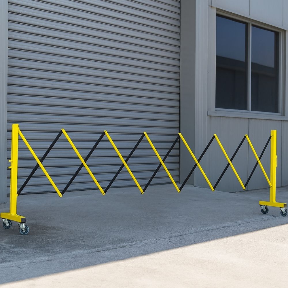 Yellow and black expandable safety barrier with castor wheels placed outdoors in front of a closed shutter door.