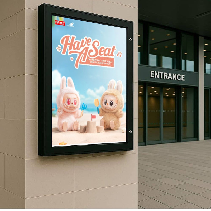 Black A0 lockable outdoor poster case wall-mounted on travertine cladding at a glass-and-steel commercial building entrance.
